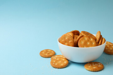 Bowl with tasty cracker biscuits on blue background