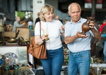 Smiling mature spouses buying retro handicrafts on flea market