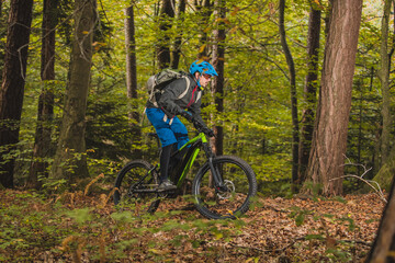 Fototapeta na wymiar Biker riding uphill with a modern electric bicycle or mountain bike in autumn or winter setting in a forest. Modern e-cyclist in woods.