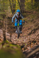 Biker riding downhill with a modern electric bicycle or mountain bike in autumn or winter setting in a forest. Modern e-cyclist in woods.