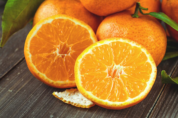 Ripe Mandarin fruit peeled open and place on old rustic look timber with group of mandarin fruits and leaves out of focus on the background