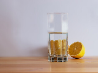 Glass of water and cut lemon are standing on the wooden desk. White background. Copy space