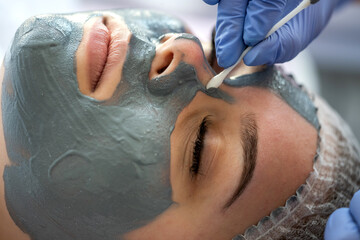 Closeup hands of a beautician in blue gloves applying beauty mask the face of a girl client
