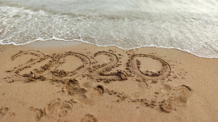 The inscription on the sand 2020 with ocean wave. the end of the terrible year caused coronavirus