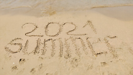 word handwritten summer 2021 on yellow sandy beach