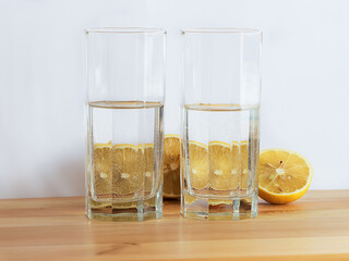 Glass of water and cut lemons are standing on the wooden desk. White background.