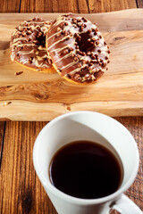 Fresh tasty chocolate with sugar icing donuts on a wooden board and a white cup with coffee. Black background. Bakery product
