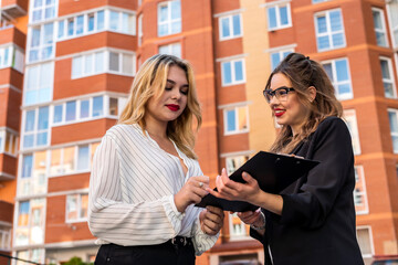Female real estate agent with clipboard key and young woman client near house for sale