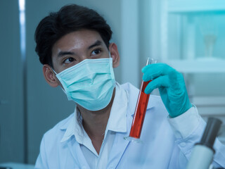 Young Asian scientist wearing mask and gloves holding red solution in the tube in the laboratory.