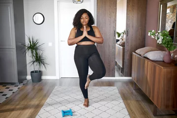 Fototapeten Junge afrikanische schwarze Frau hält das Gleichgewicht, steht auf einem Bein, Yoga-Zeit zu Hause. konzentriert auf Yoga, Meditation © Roman