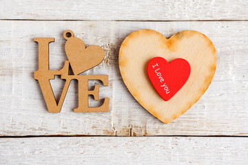 Letters made of wood with the text Love and two hearts with the text I love you on a white wooden background.