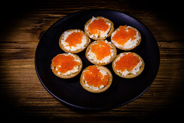 Tartlets with red caviar on a black plate. Festive food