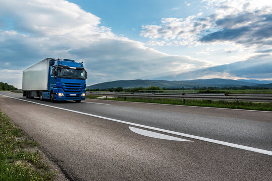 Blue semi trailer truck on a highway driving at bright sunny sunset. Transportation vehicle