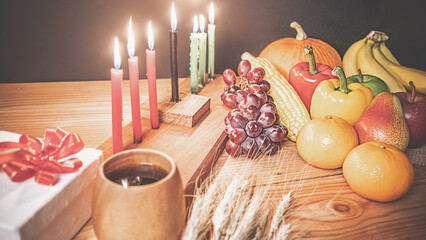 Obraz na płótnie Canvas Kwanzaa holiday concept with decorate seven candles red, black and green, gift box, pumpkin,corn and fruit on wooden desk and black background.