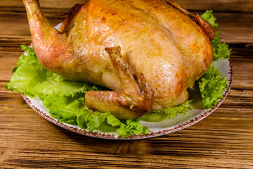 Plate with roasted whole chicken and lettuce leaves on a wooden table