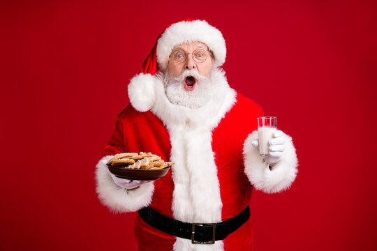 Photo of amazed crazy santa claus hold x-mas breakfast ginger bread cookies plate milk glass wear red costume isolated over bright shine color background - Powered by Adobe
