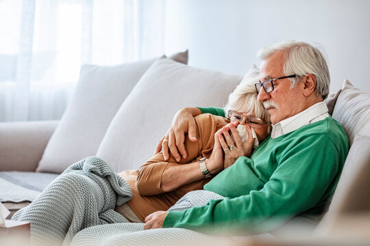 Flu senior couple under the blanket with pills , flu and cold concept with medicines. Elderly couple lying on the bed and blow their nose , flu concept with tissues and blanket
