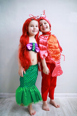 Children in smart carnival costumes on a plain background. Costume of sea fairy creatures. Mermaid and crab.