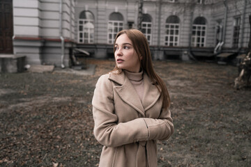 Fototapeta premium a girl warms her hands in her sleeves, a beautiful girl stands in a field dressed in a coat