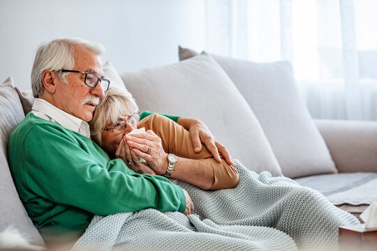 Couple of old aged senior people at home with seasonal winter cold illness disease sit down on the sof together forever - health problems for retired man and woman with white hair