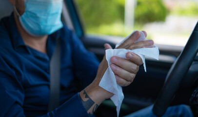 man disinfecting his hands with wipes inside the car