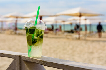 Mojito cocktail on wooden table with sandy beach on a background
