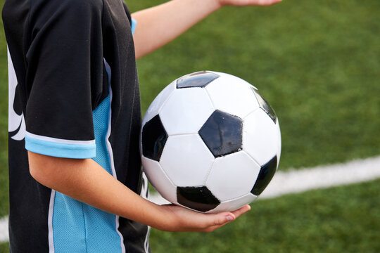 close-up photo of ball in hands of football player, cropped child boy in uniform going to play