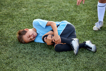 little caucasian boy fell to his knee, ache in joints during football game outdoors, injury during sport competition © Roman