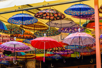 Many umbrellas hanging from the ceiling in street cafe