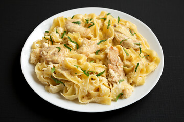 Homemade Chicken Fettuccine Alfredo on a white plate on a black background, low angle view.
