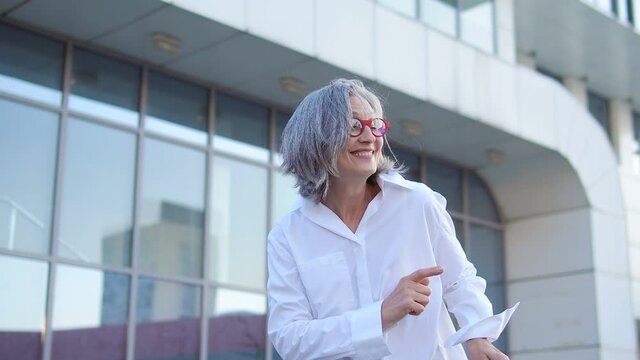 Happy positive gray haired lady dancing outdoor, celebrating successful startup