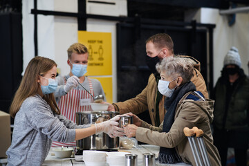 Volunteers serving hot soup for homeless in community charity donation center, coronavirus concept.