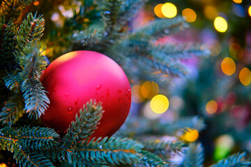 Obraz na płótnie Canvas Red ball as decoration for New Years celebration, yellow bokeh. Winter christmas tree with bauble, copy space