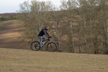 Sports brutal bearded guy on a modern mountain bike. Cyclist on the green hills in the spring.