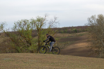 Obraz premium Sports brutal bearded guy on a modern mountain bike. Cyclist on the green hills in the spring.
