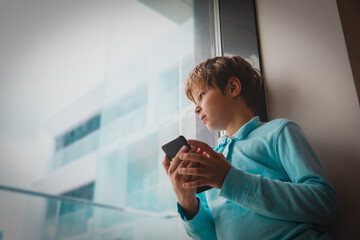 Boy looking outside while staying home with mobile phone, social distancing challenges