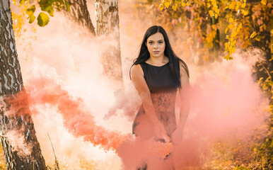 Beautiful girl on a background of colored smoke. Smoke screen in the woods. Young woman in forest having fun with smoke grenade, bomb.