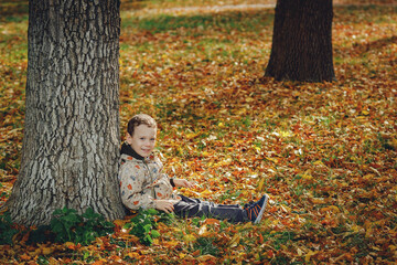 child sitting under a tree in autumn forest