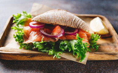 Healthy sandwich with rye bread bun, salmon, avocado, onion and salad served on a wooden rustic board.
