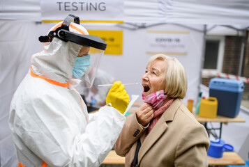 Senior woman in covid-19 testing center outdoors on street, coronavirus and swab taking concept.