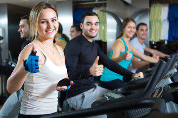 Fototapeta premium Smiling active young adults training on exercise bikes in gym.