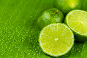 Close up pile of half and whole fresh lime juicy on green banana leaves with clearly water drop on surface