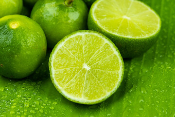 Close up pile of half and whole fresh lime juicy on green banana leaves with clearly water drop on...
