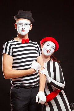 Portrait of two mime artists performing, isolated on black background. Man is standing straight and woman nestled against him. Symbol of warm relationships, friendship, trust