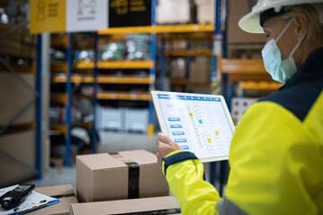 Young worker with tablet working indoors in warehouse, coronavirus concept.