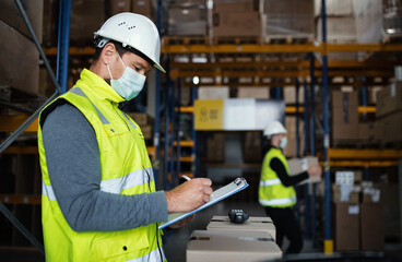 Man worker with clipboard working indoors in warehouse, coronavirus concept.