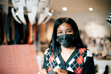 portrait of a black female shopkeeper at work wearing a protective face mask against viruses. New...