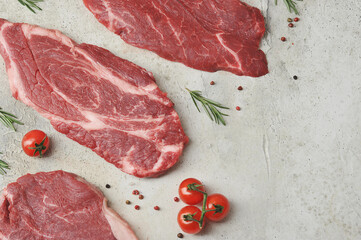 Beef steaks on a light background.  Rosemary, spices and cherry tomatoes complete the composition.  View from above.  Free space for text placement.