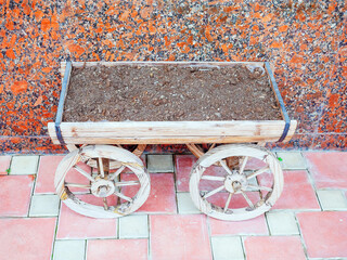 A decorative plant pot in the form of a wooden cart with soil stands near a marble wall