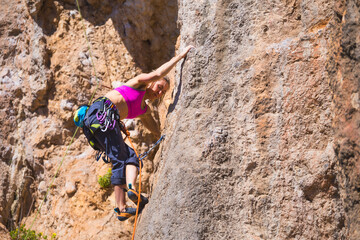 A strong woman climbs a beautiful orange rock.